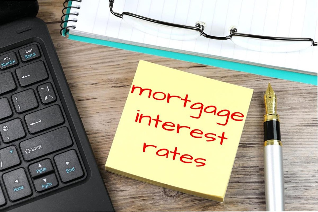 En närbild av en arbetsyta med en gul kom-ihåg-lapp där det står 'mortgage interest rates', vilket illustrerar vikten av noggrann ekonomisk planering för bolån.